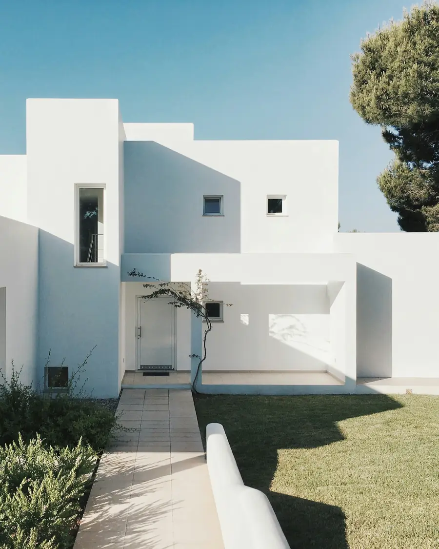 Casa unifamiliar mediterránea de fachada blanca junto a un pino, con jardín y acceso peatonal