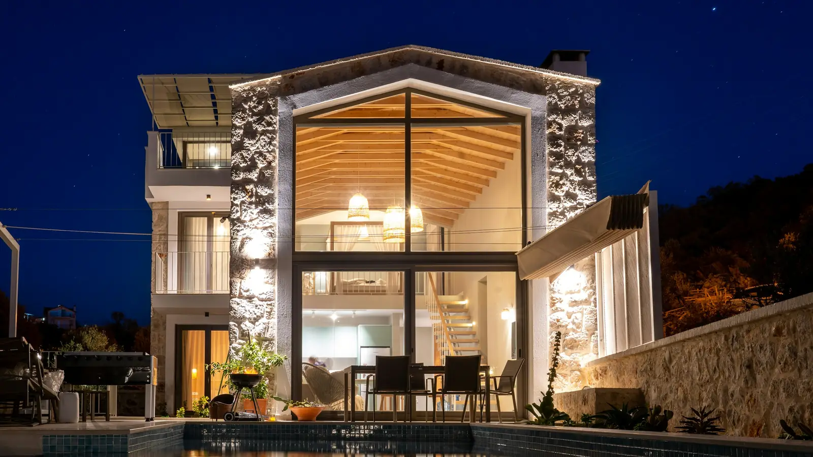 Fachada de una casa iluminada de noche reflejada en la piscina