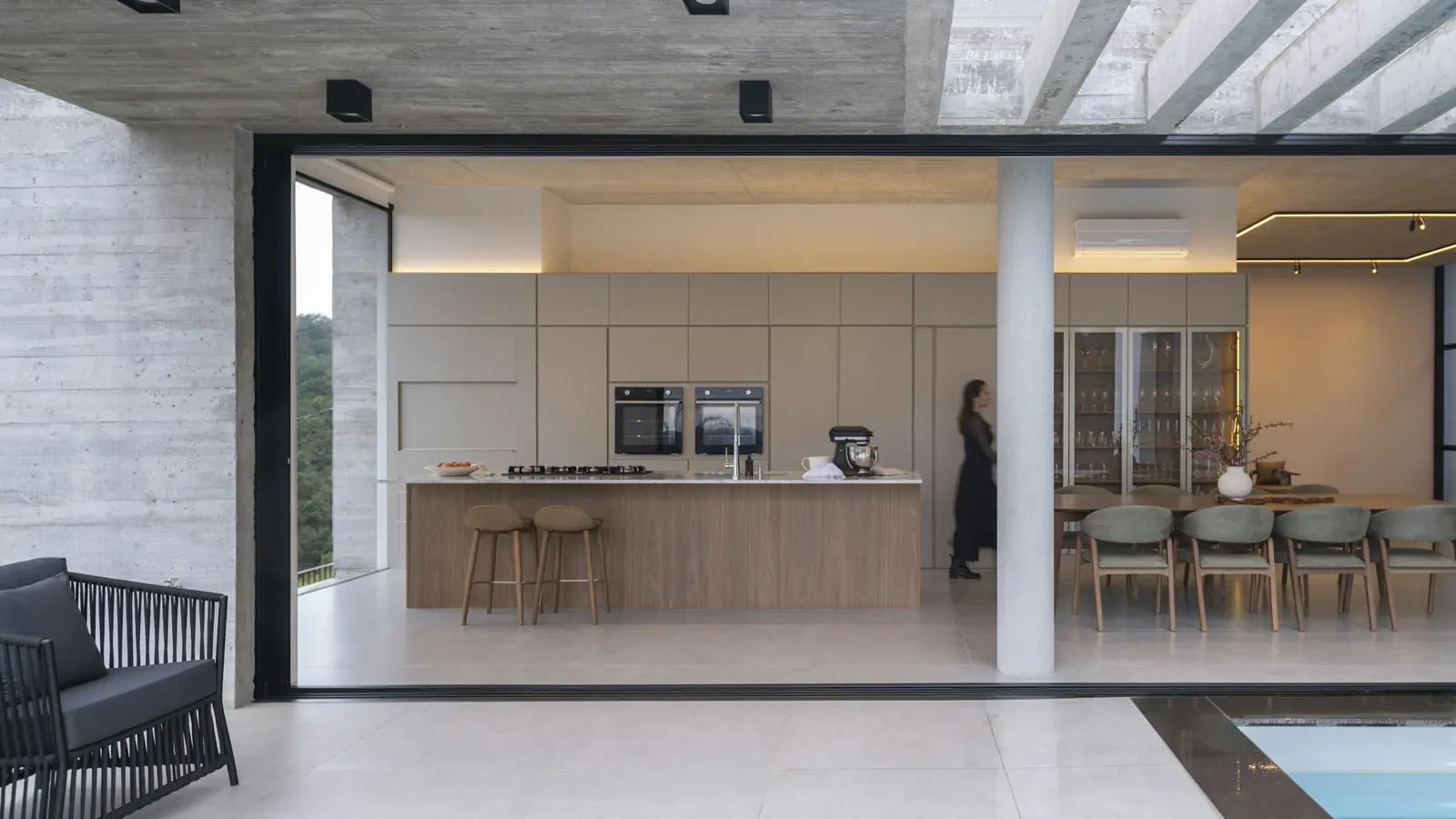 Cocina abierta con isla de madera y comedor que se abren a la terraza y la piscina