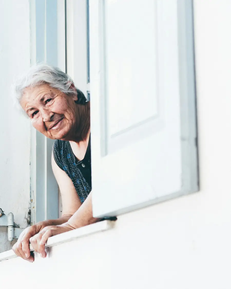 Mujer mayor sonriente asomada a la ventana de su casa
